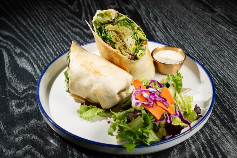 Hummus falafel wrap cut in half with a side salad and dressing