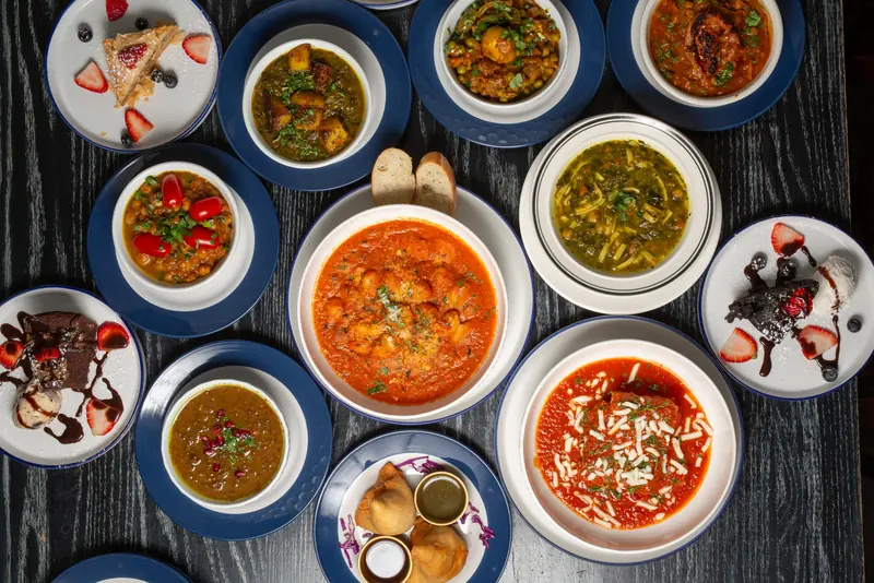 Bowls of Sage's vegetarian stews, Osh soup and desserts on a dark wood table
